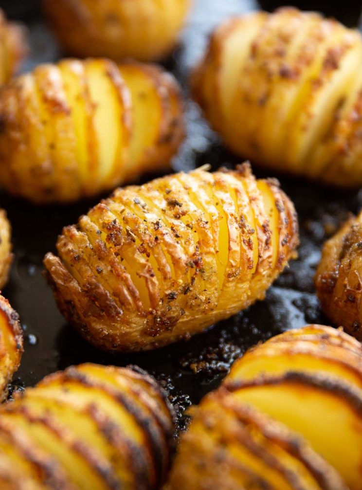 closeup shot of hasselback potatoes on black baking tray fresh out the oven