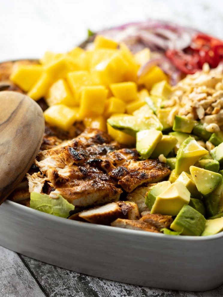 closeup shot of chicken in salad in heart shaped bowl with wooden salad tossers resting on side