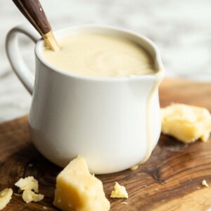 cheese sauce in small white jug with gold spoon digging in