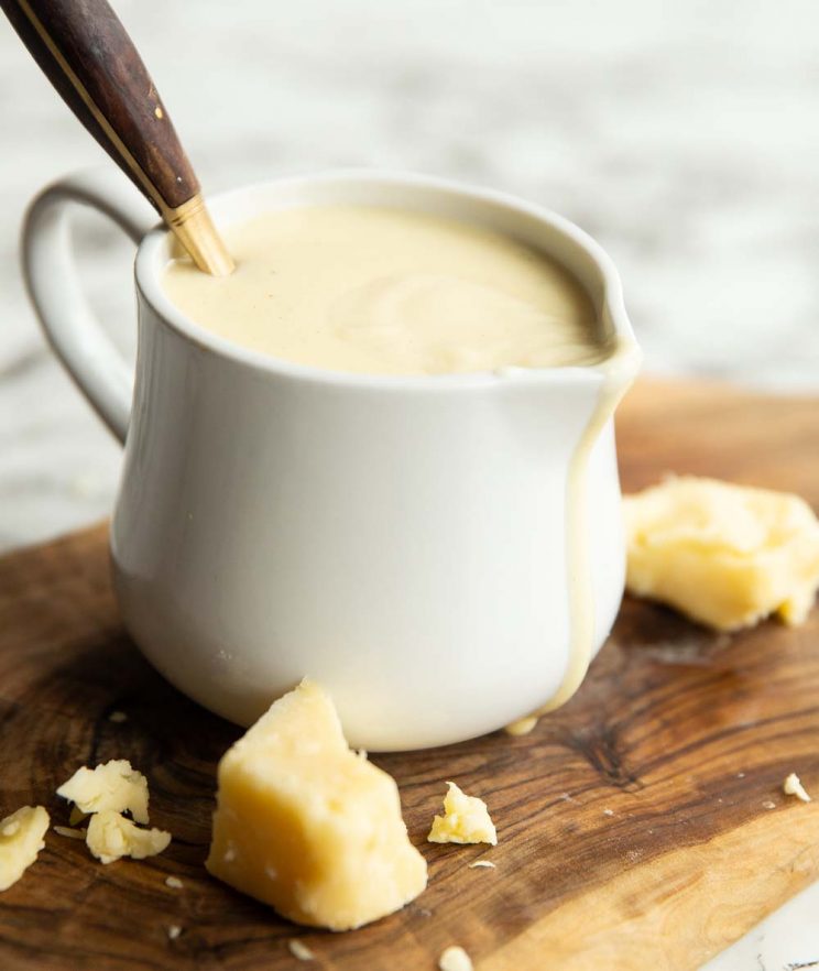 cheese sauce in small white jug with gold spoon digging in