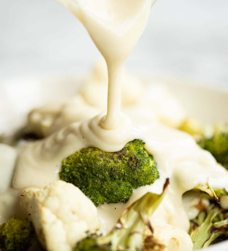pouring cheese sauce over roasted broccoli
