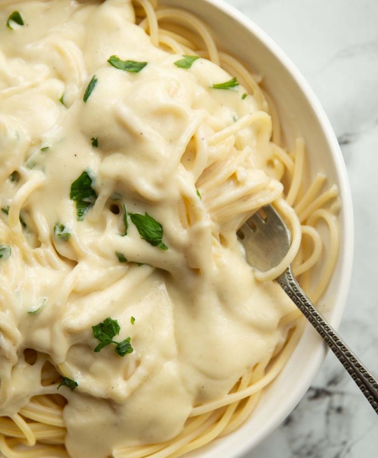 overhead shot of cheese sauce poured over spaghetti garnished with parsley