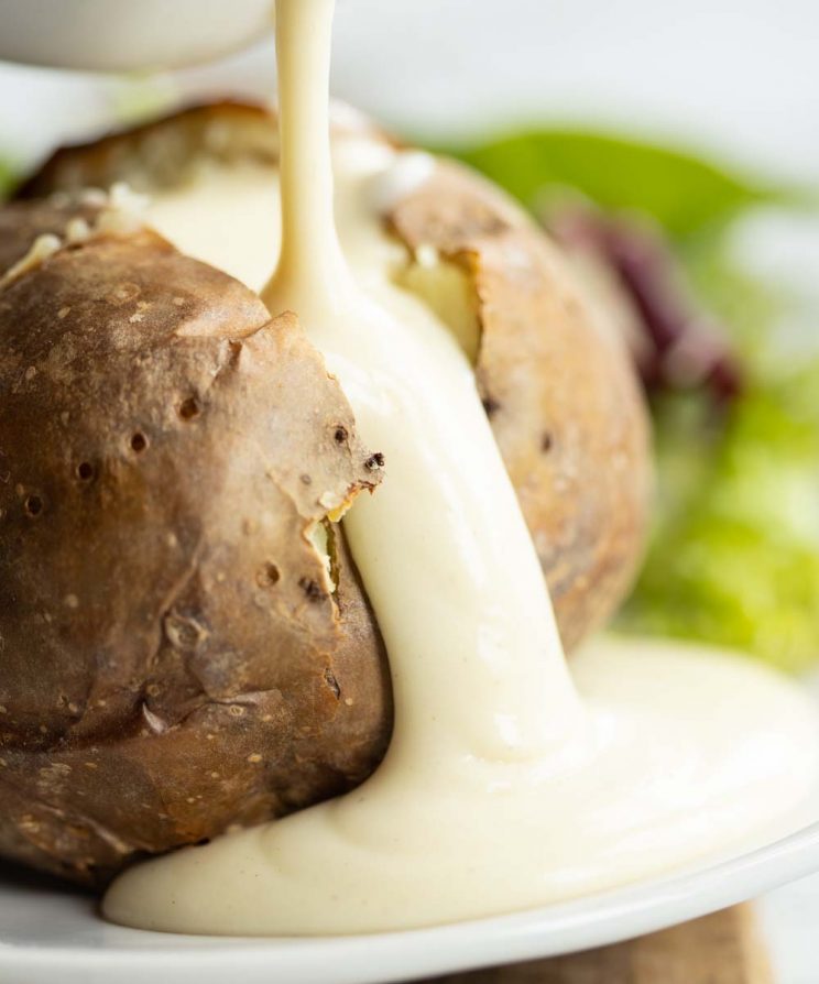pouring cheese sauce over large sliced open baked potato