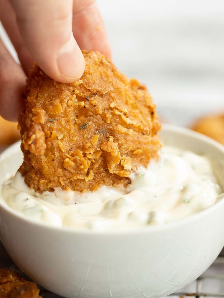 hand dunking potato into small white pot of creamy dip