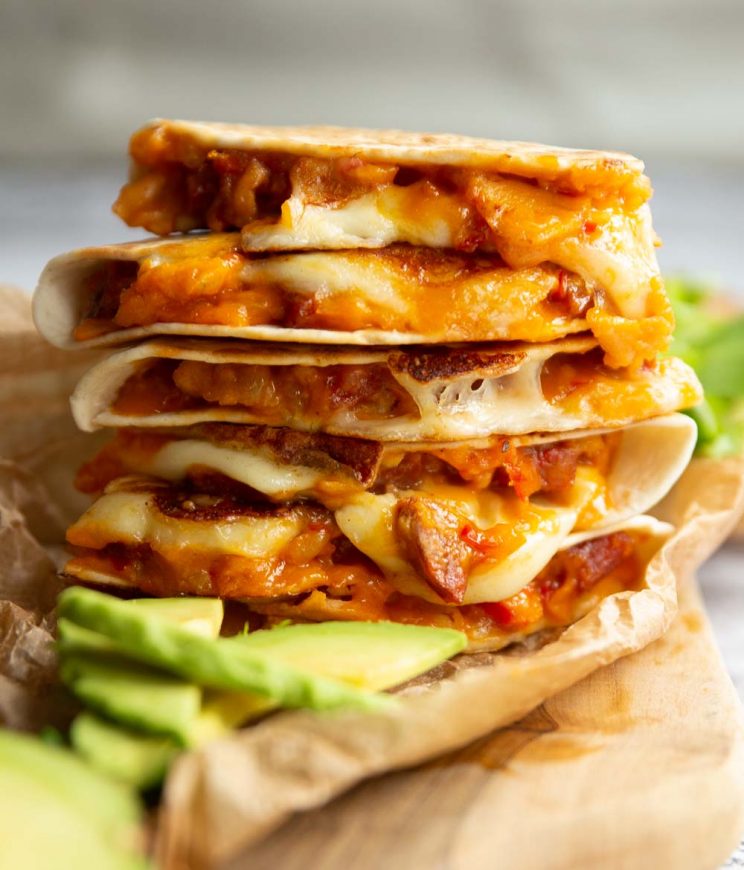 quesadillas stacked on each other on wooden board served with avocado slices and side salad 