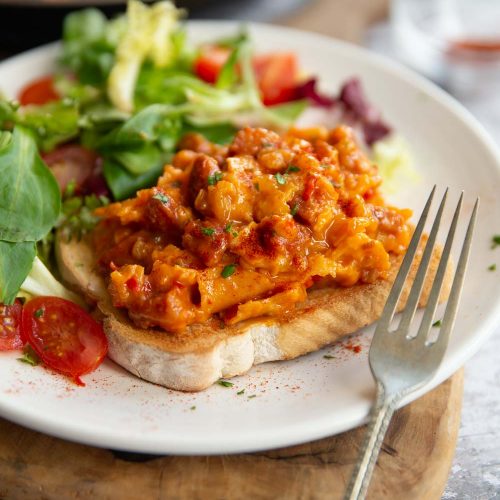 scrambled egg on slice of toast with side salad on white plate