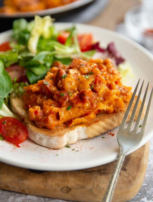 scrambled egg on slice of toast with side salad on white plate