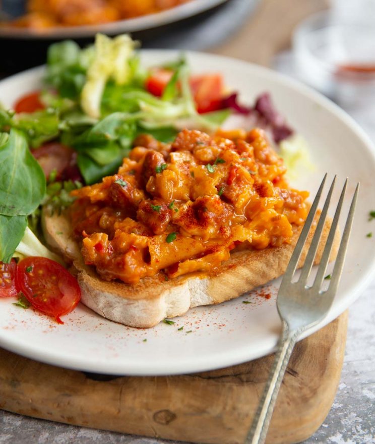 scrambled egg on slice of toast with side salad on white plate