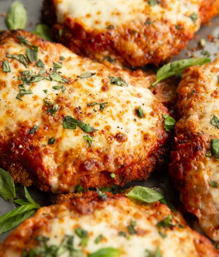 close up shot of chicken parmas fresh out the oven garnished with basil