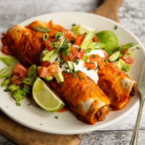two enchiladas on white plate with sour cream and other toppings