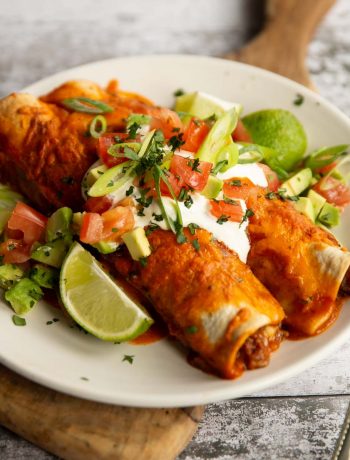 two enchiladas on white plate with sour cream and other toppings