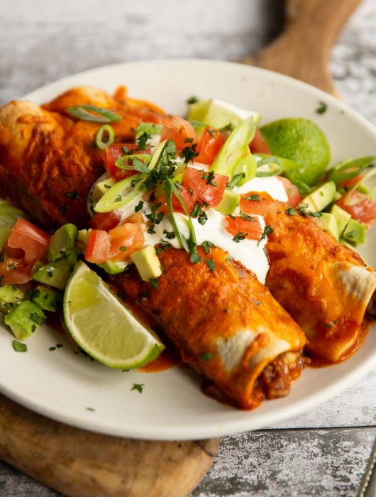 two enchiladas on white plate with sour cream and other toppings