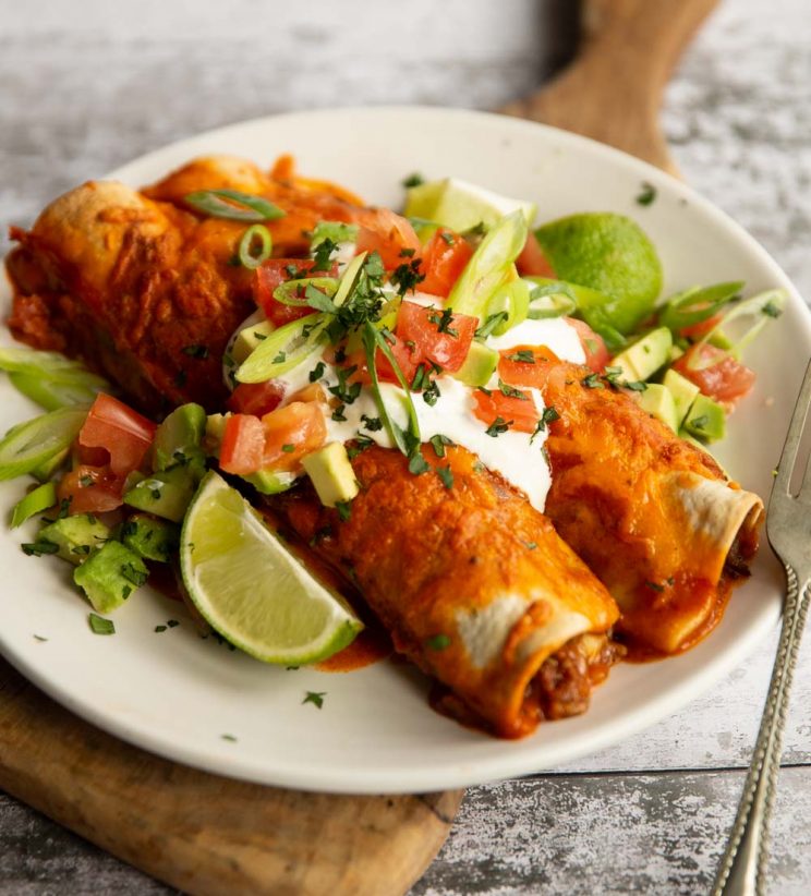 two enchiladas on white plate with sour cream and other toppings