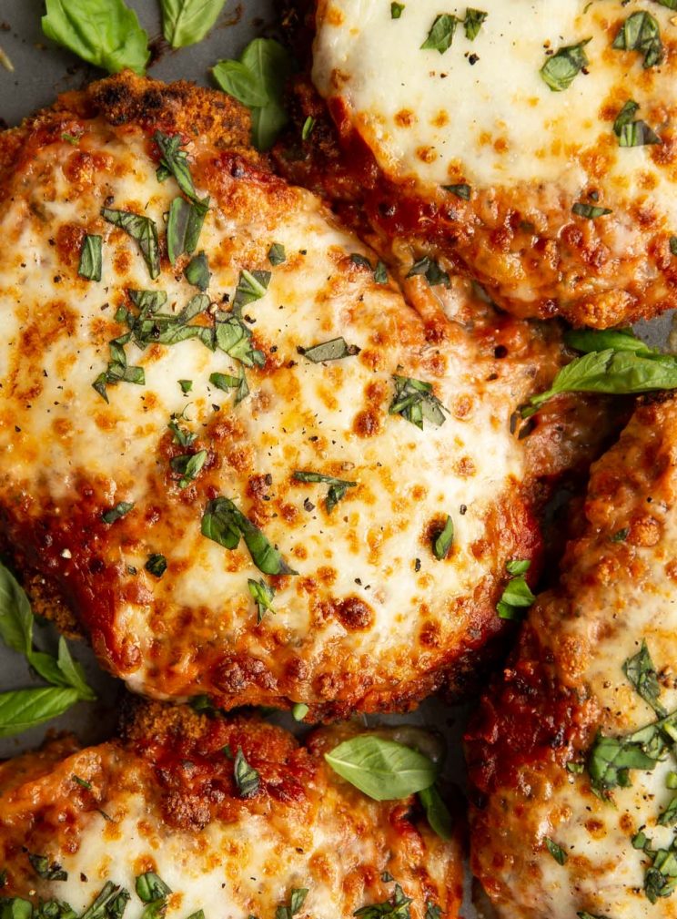 overhead shot of chicken parmesan fresh out the oven garnished with chopped and whole basil leaves