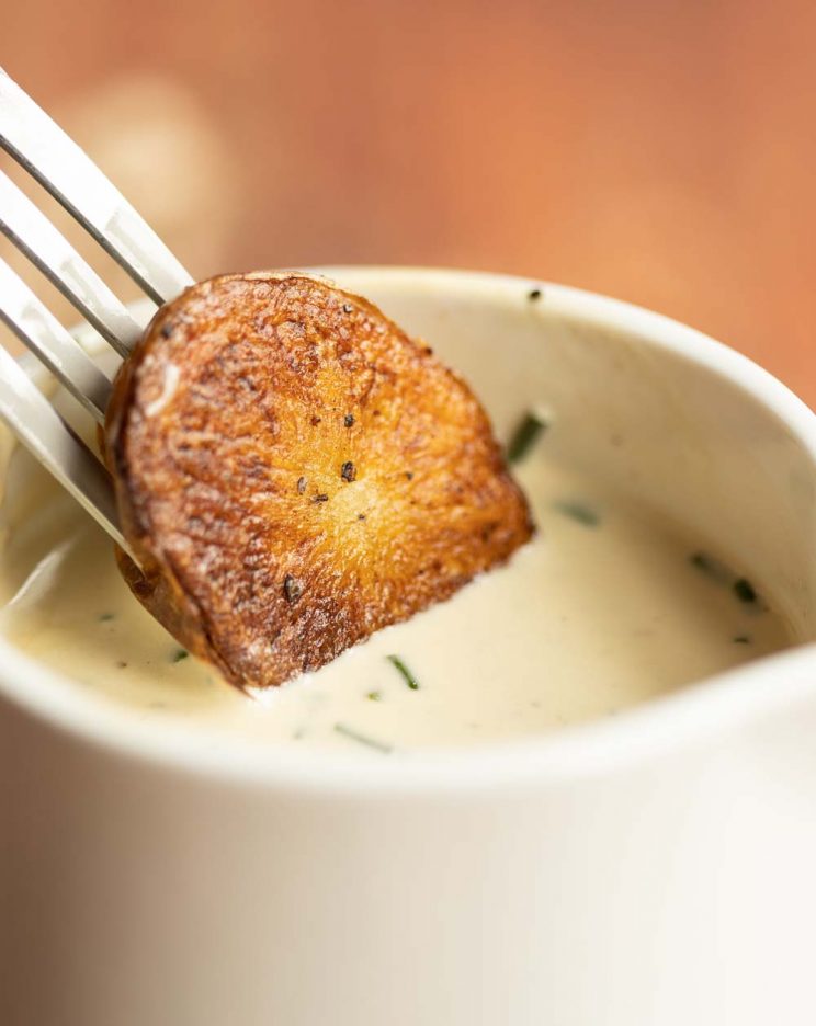 fork dipping roast potato into small jug of sauce
