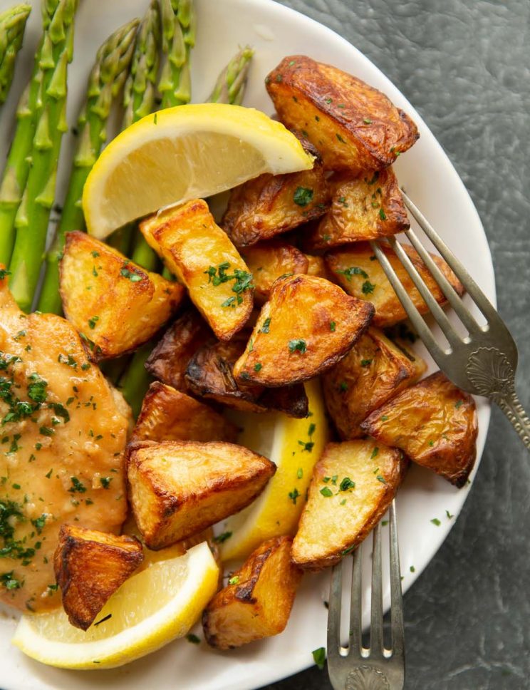 overhead shot of potatoes served on white plate with asparagus and chicken with two silver forks