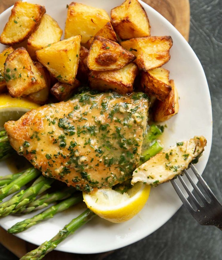 overhead shot of chicken served with potatoes and asparagus on white plate