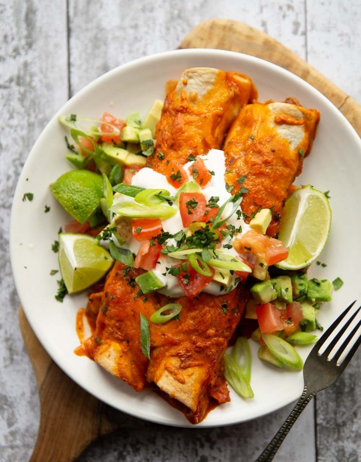 overhead shot of two enchiladas on white plate with toppings