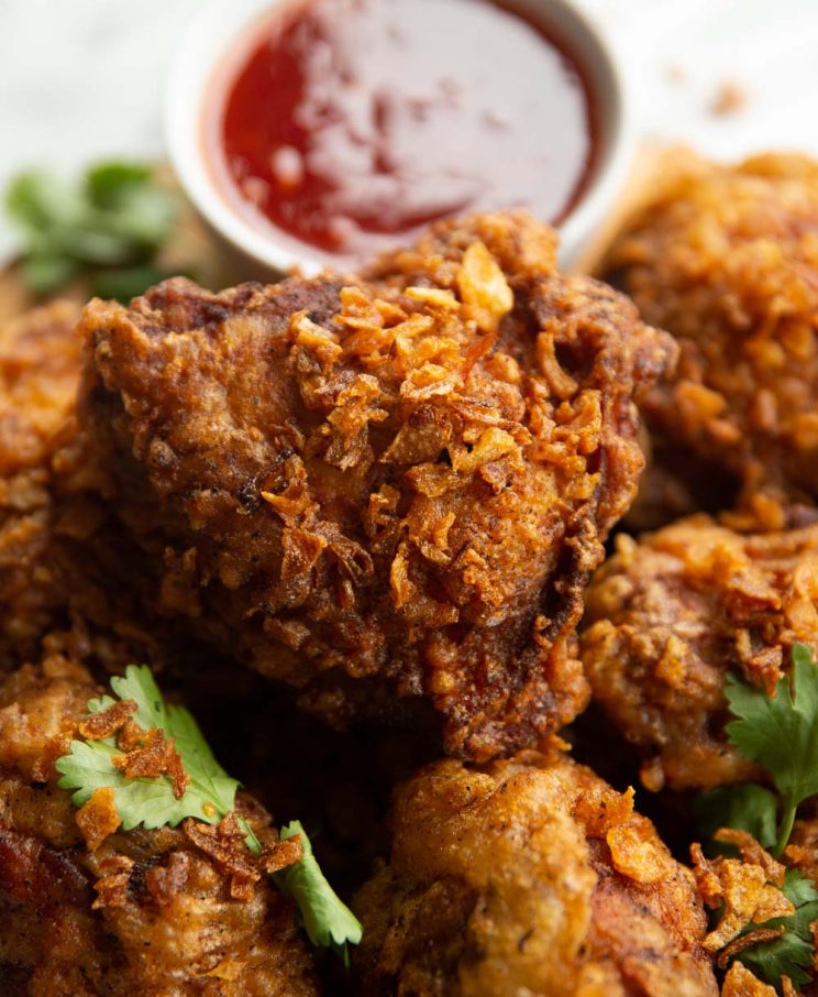 close up shot of fried chicken sprinkled with fried shallots with dip blurred in background