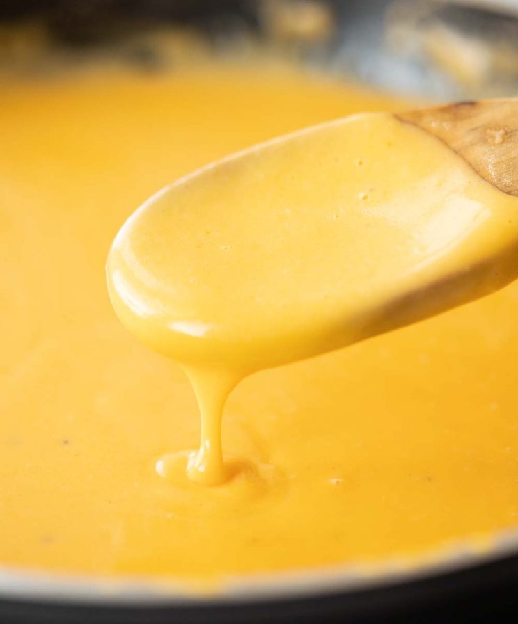close up shot of wooden spoon scooping nacho cheese sauce out of pan