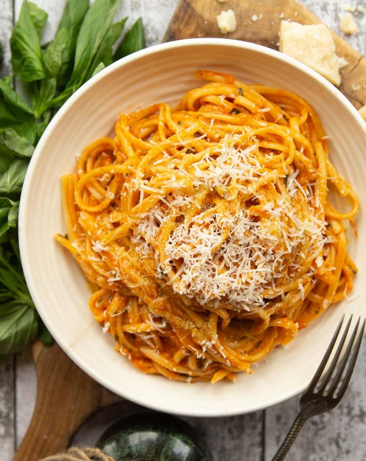 overhead shot of pasta in white bowl with fresh basil and parmesan surrounding