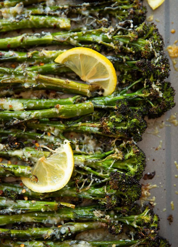 overhead shot of broccolini on grey oven tray with lemon wedges
