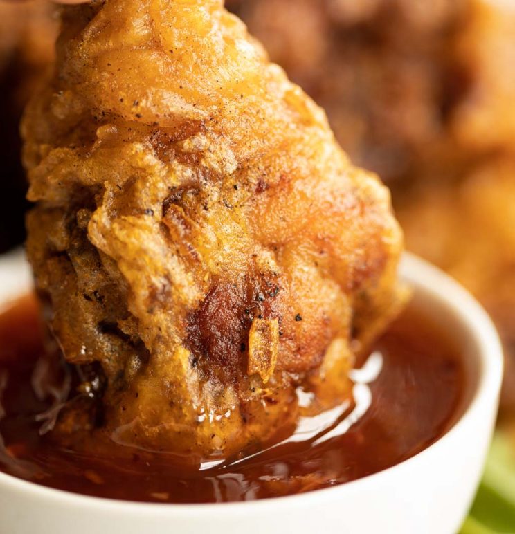 close up shot of chicken drum stick dunking into small white pot of sweet chilli sauce