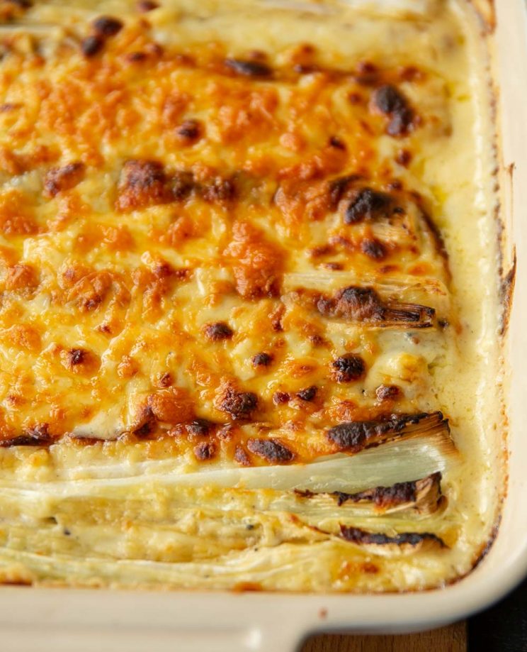 closeup shot of cheesy leeks fresh out the oven in white baking dish