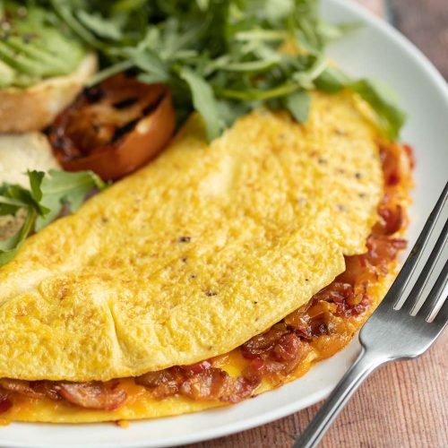 closeup shot of omelette on white plate with silver fork resting on it with salad blurred in background