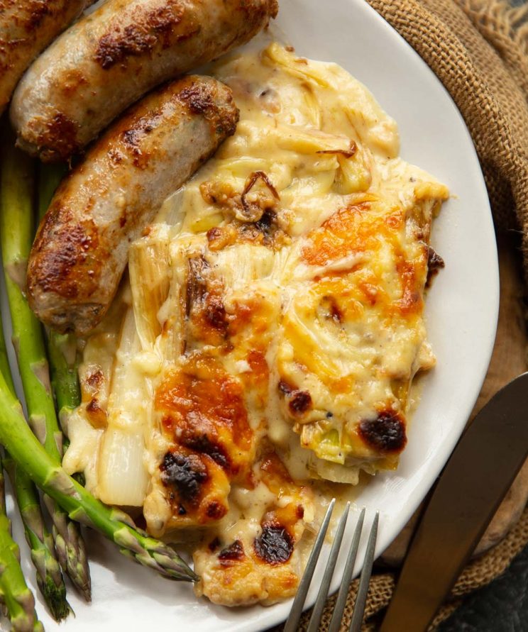 overhead shot of leeks served on white plate with sausages and asparagus