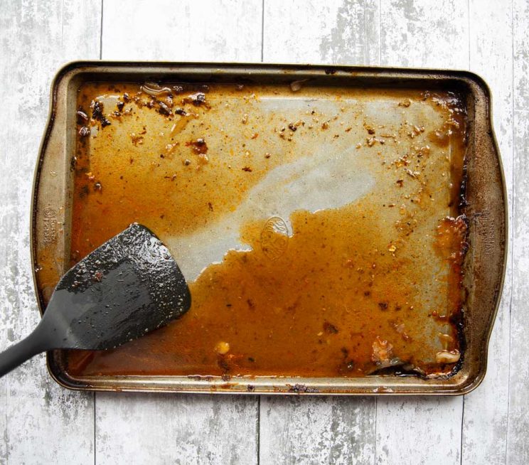overhead shot of plastic spatula scraping flavour off large silver tray