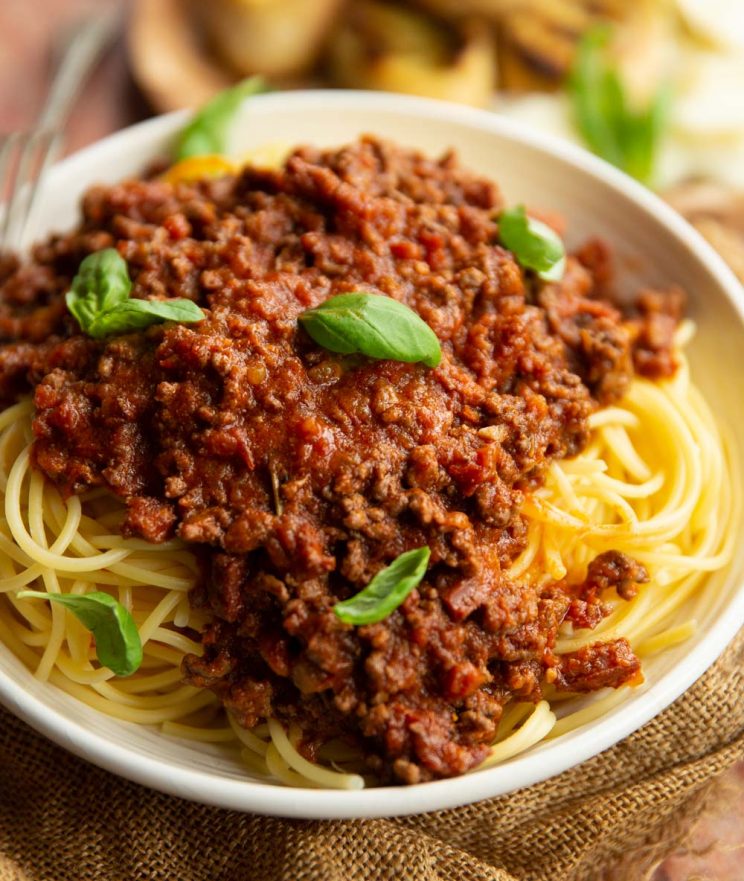 close up shot of bolognese served on spaghetti garnished with small basil leaves