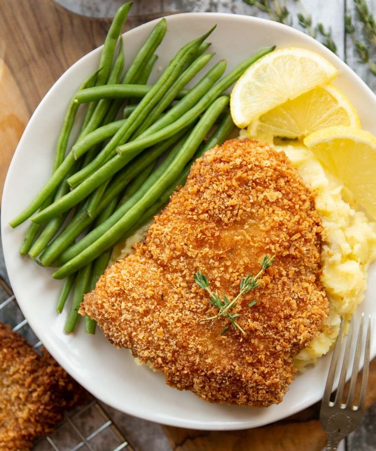 overhead shot of schnitzel on white plate served with mash, green beans and lemon