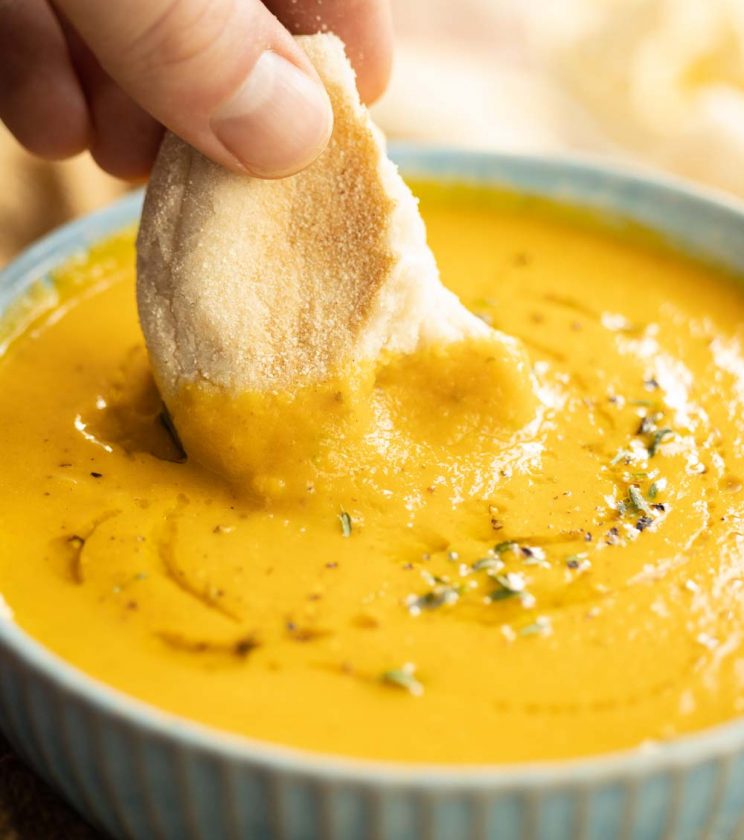 closeup shot of dunking bread into a small bowl of carrot soup