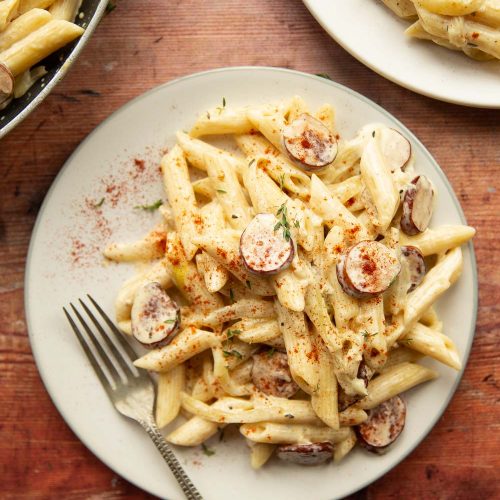 overhead shot of pasta on white plate with silver fork on wooden background