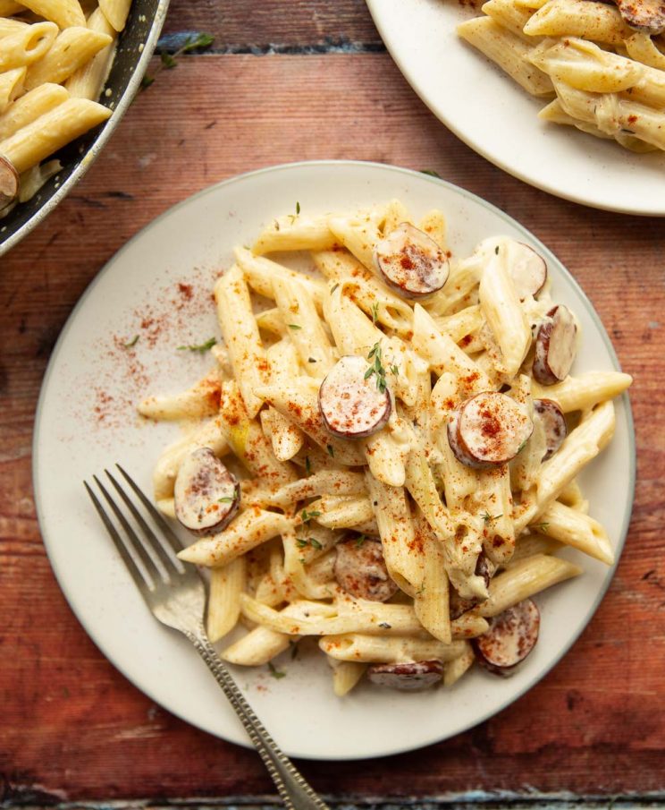 overhead shot of pasta on white plate with silver fork on wooden background