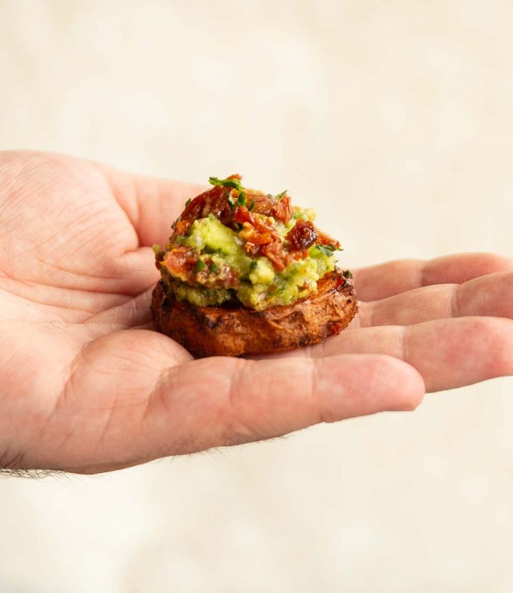 mini sweet potato bite in palm on hand against white backdrop