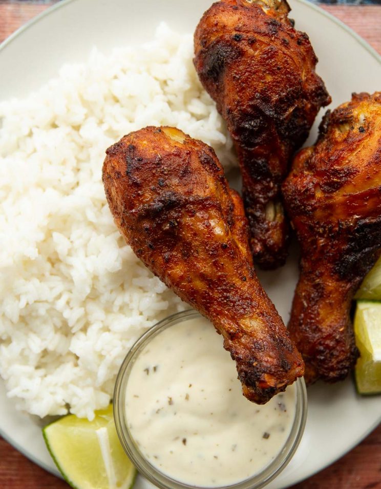 overhead shot of 3 drumsticks on white plate served with rice, ranch and lime wedges