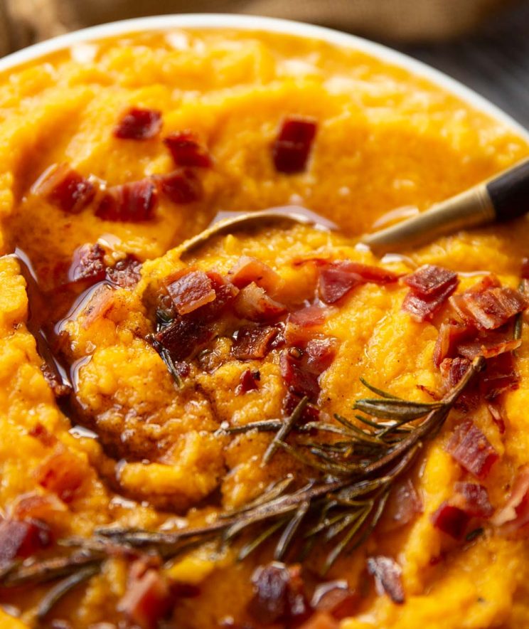 closeup shot of spoon digging into mash garnished with rosemary and bacon