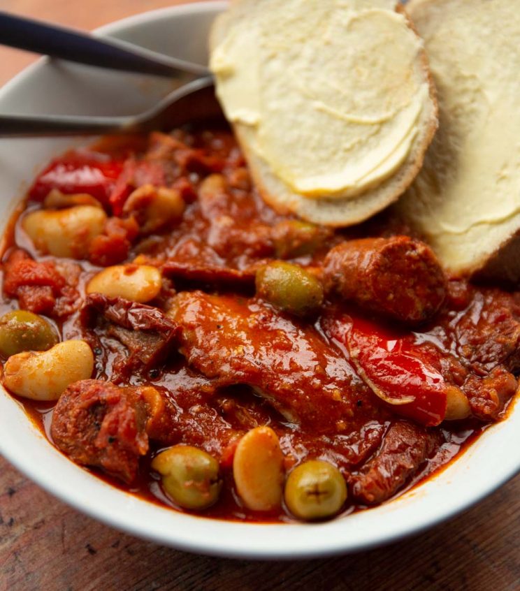 close-up of chicken and chorizo in a large white bowl served with two slices of buttered bread