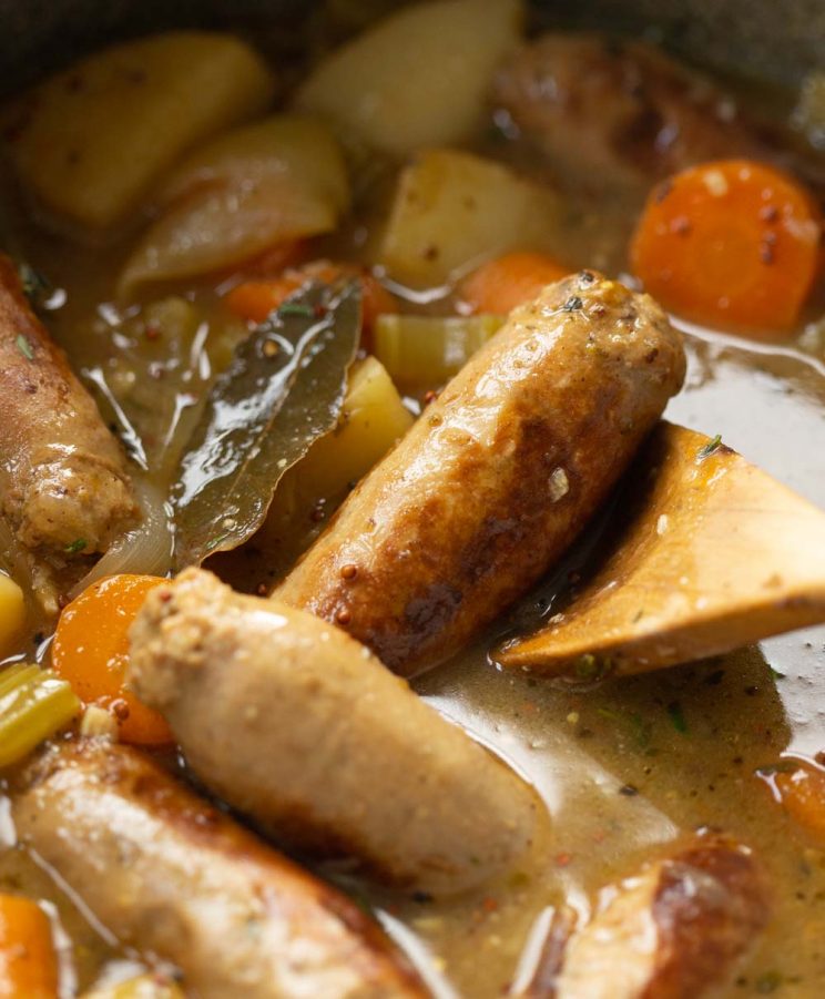 closeup shot of wooden spoon lifting up sausage in casserole dish