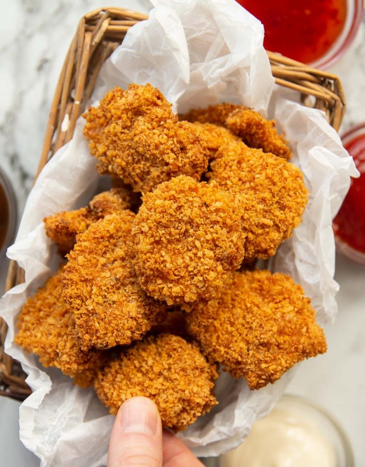 overhead shot of nuggets in small box surrounded by dip with fingers taking one off the top