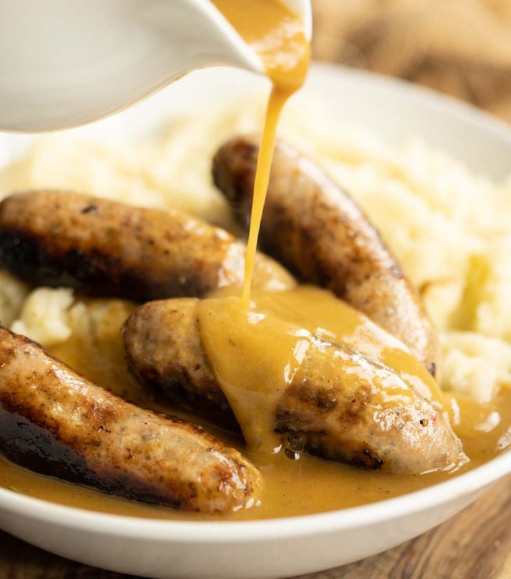 pouring gravy over sausages on mashed potato in white bow