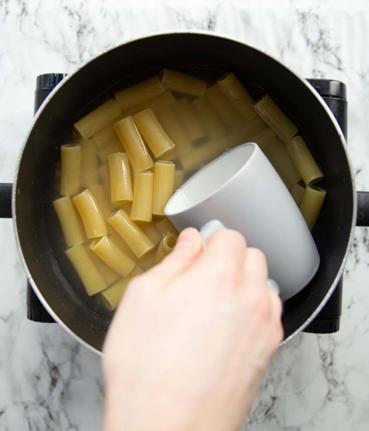 grey mug scooping into boiling pasta to collect water