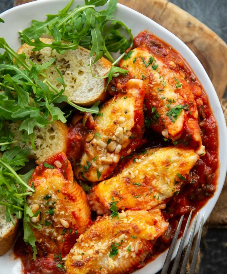 overhead shot of 5 stuffed shells of plate with garlic bread and rocket