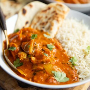 curry in a large white bowl with rice and flatbread and gold spoon digging in