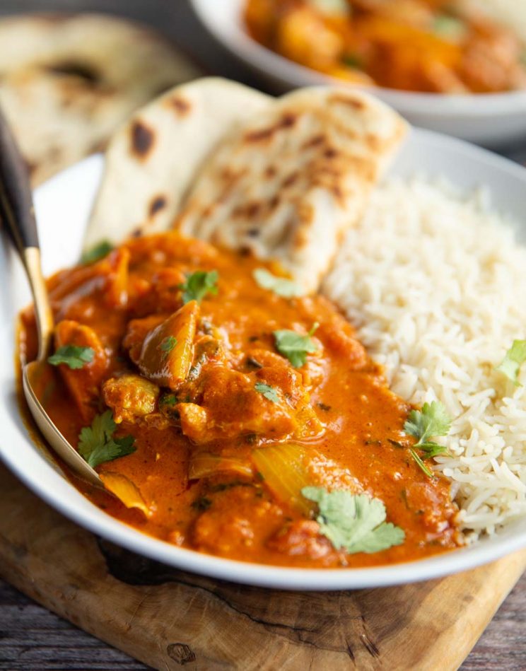 curry in a large white bowl with rice and flatbread and gold spoon digging in