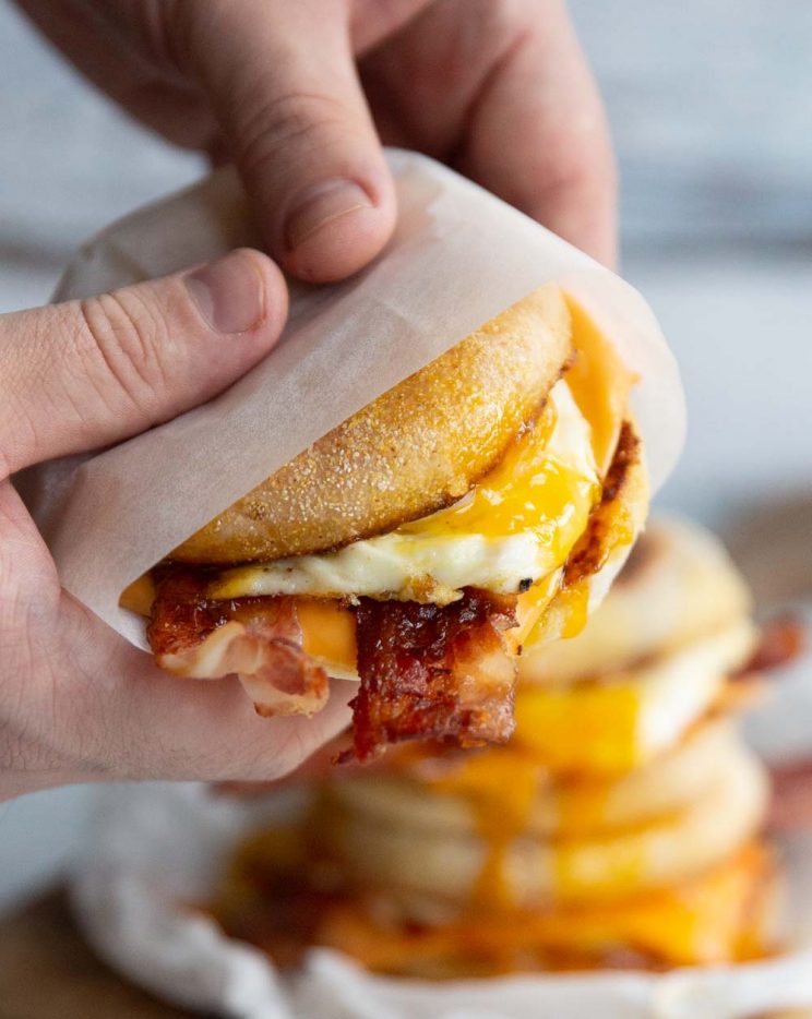 two hands holding sandwich wrapped in parchment paper with more blurred behind