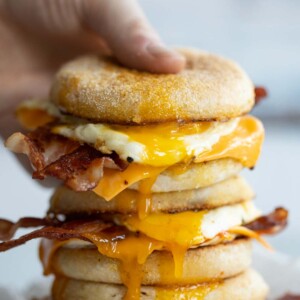 hand grabbing top sandwich of a stack with yolk dripping out
