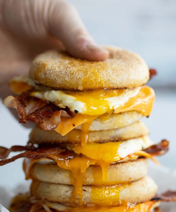hand grabbing top sandwich of a stack with yolk dripping out